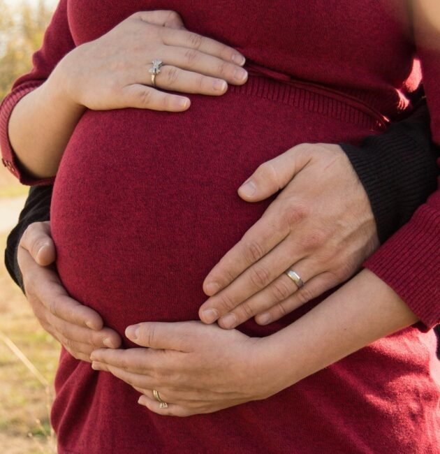pregnant woman standing behind the man holding tummy